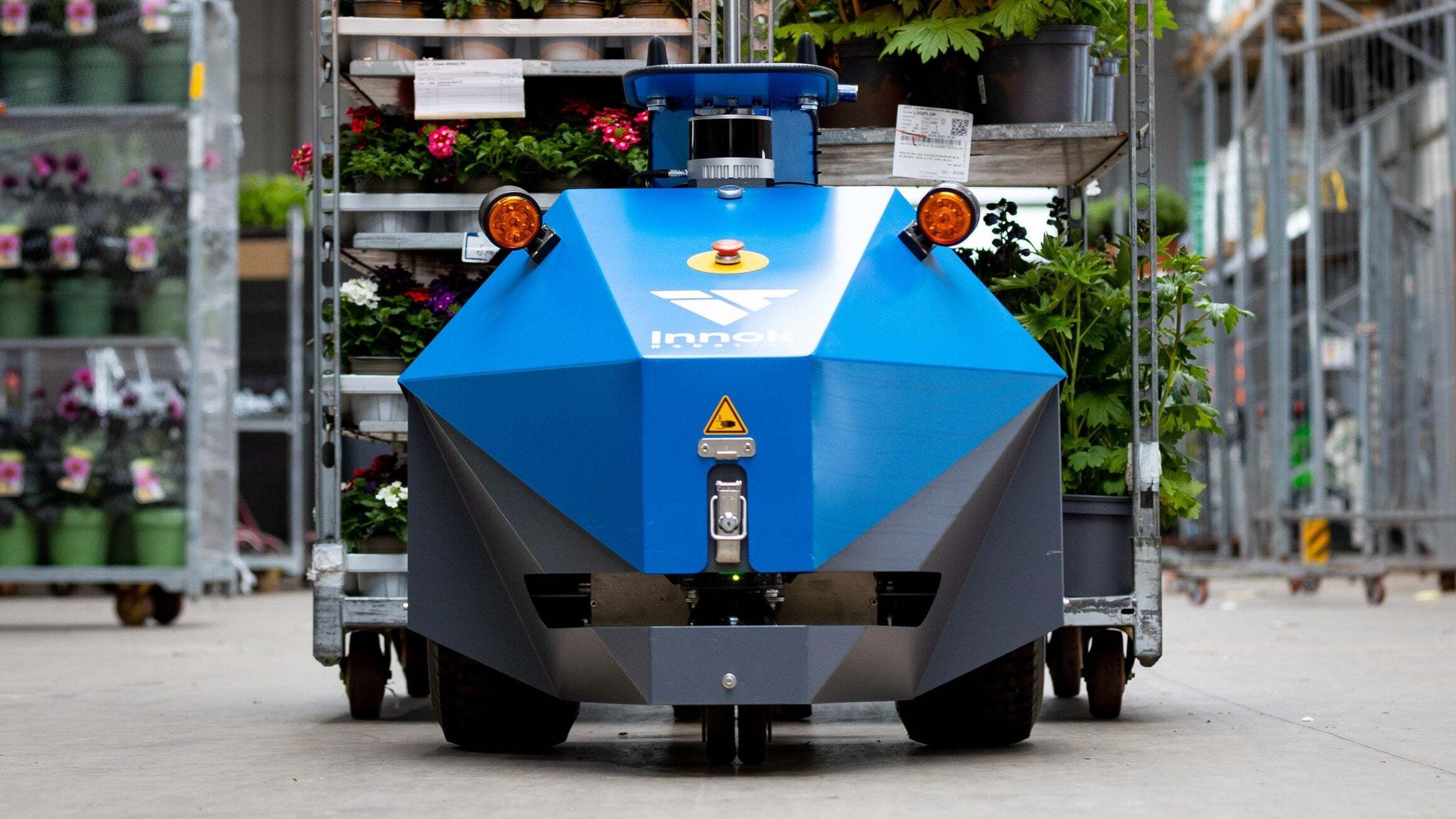 Autonomer Transportroboter INDUROS in Frontansicht vor einem Rollwagen mit Pflanzen in einer Halle