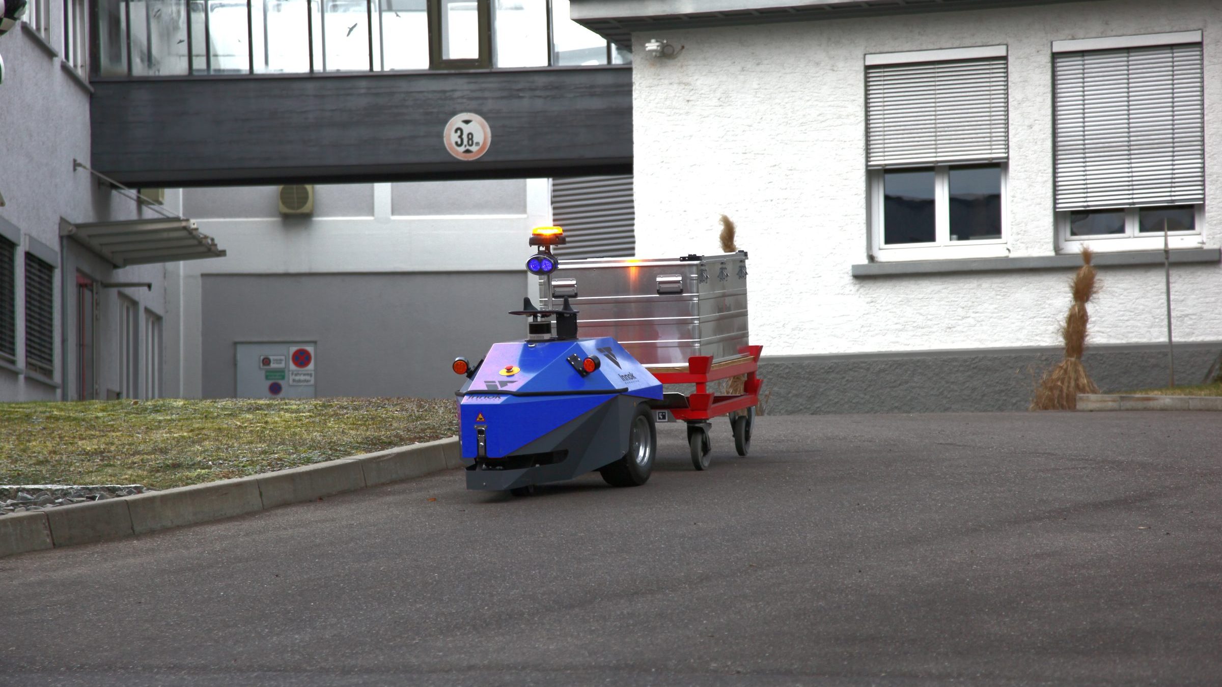 Autonomer Transportroboter INDUROS mit Anhänger auf einem Werksgelände zwischen Industriegebäuden